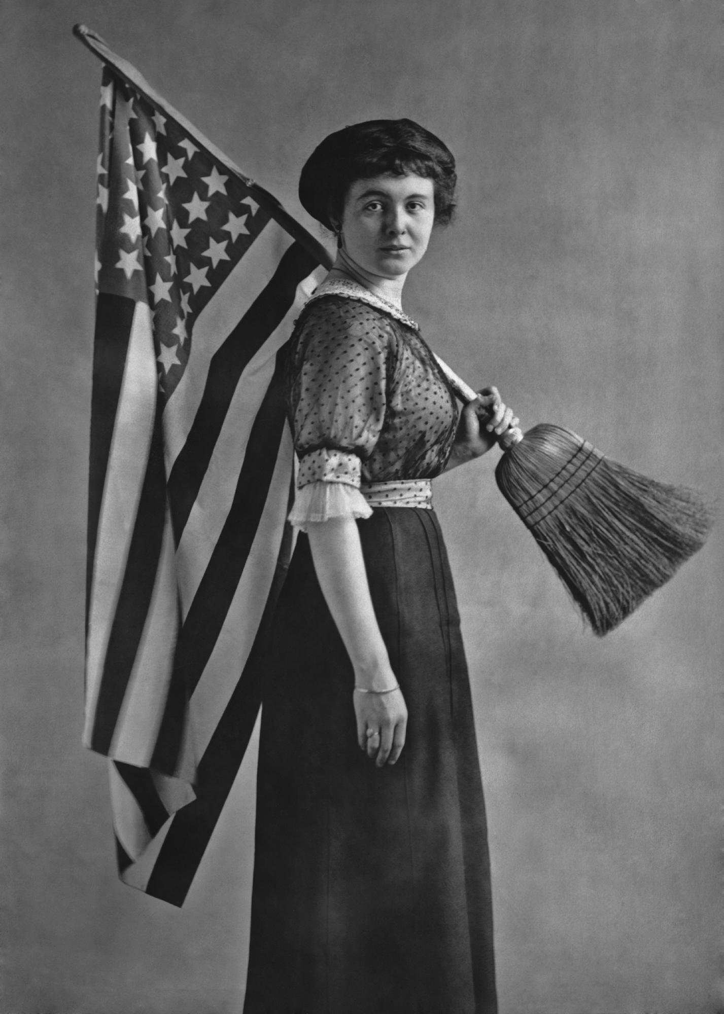 Suffragette posing with an American flag attached to a broom handle. Circa 1917.jpg