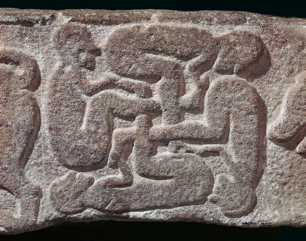 Detail of Meigle no. 26, a recumbent gravestone made of sandstone, depicting a swastika of four interlaced naked human figures. 9th-10th century CE, now on display at the Meigle Sculptured Stone Museum in Scotland.jpg