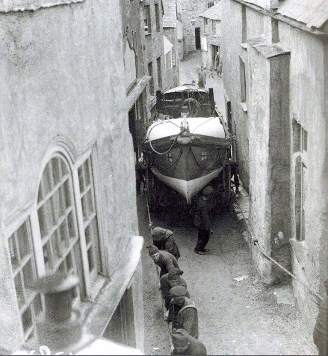 Sailors pull a boat through the narrow streets of the town of Port Isaac from its construction site for launching. England, 1928.jpg
