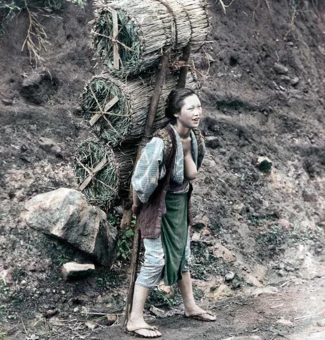A very cheerful Japanese woman carrying three huge tawara (rice straw bags) filled with charcoal on what appears to be a lonely country road. c.1890.jpg