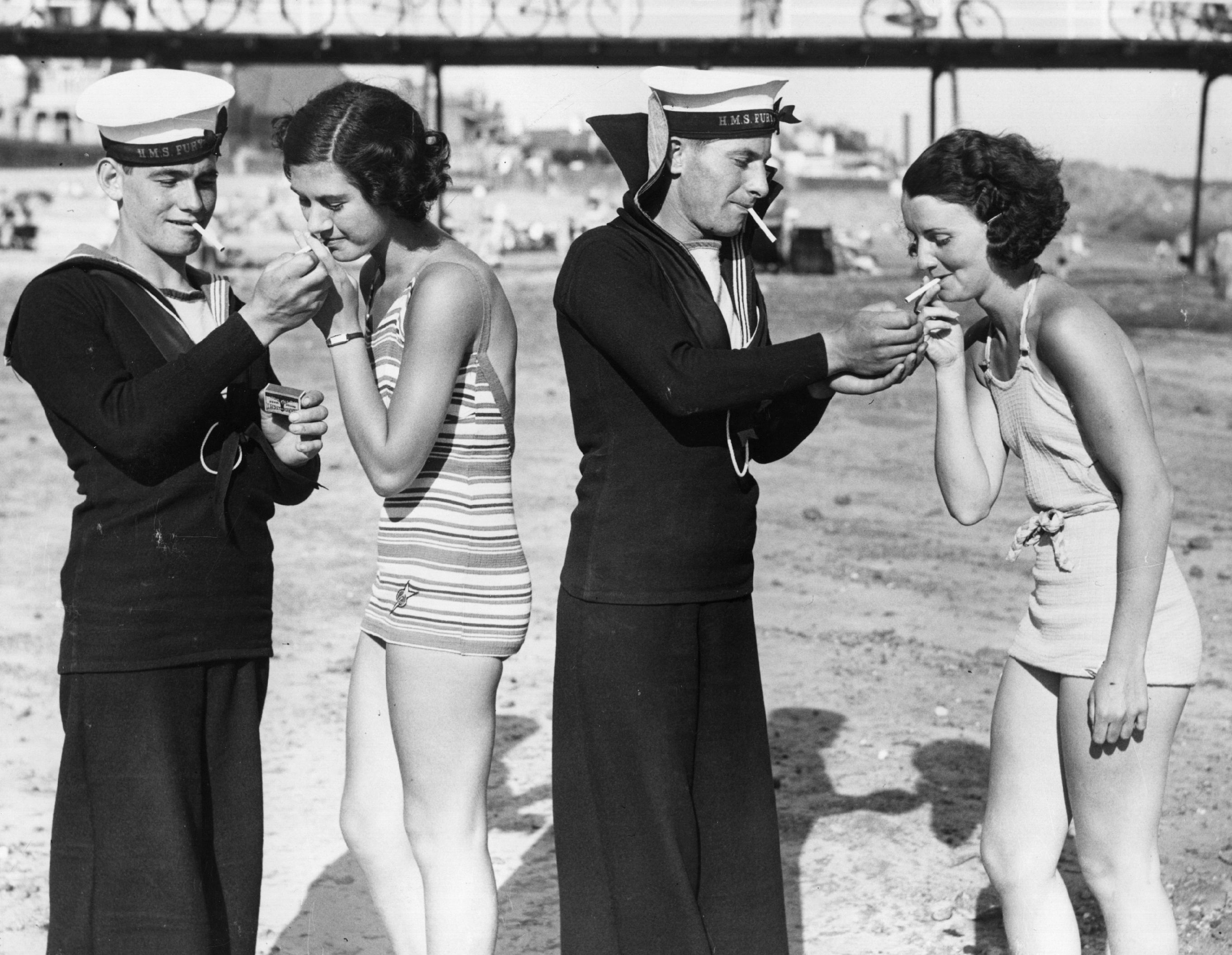 Two sailors from HMS Fury enjoy a smoke with two women in bathing suits on a beach in Jersey (Photo by William Vanderson), 29th June 1935.jpg