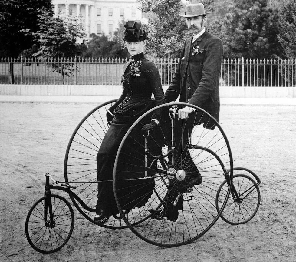 Well-dressed couple seated on a bicycle for two. 1911.jpg