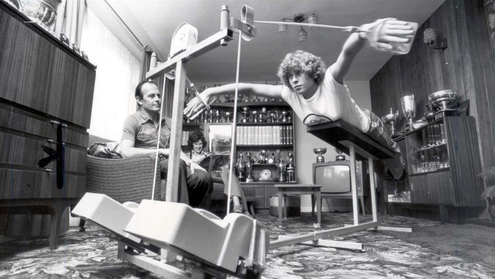 Sharon Davies practicing the butterfly stroke at home in Devon, as her father and brother look on, 1978.jpg