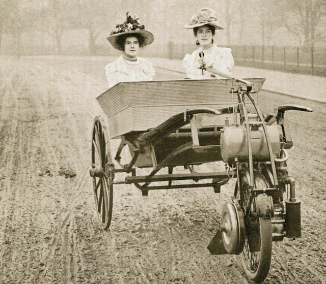 Two young ladies driving and riding in a Lawson’s Motor Wheel of 1902, London, c. 1908.jpg