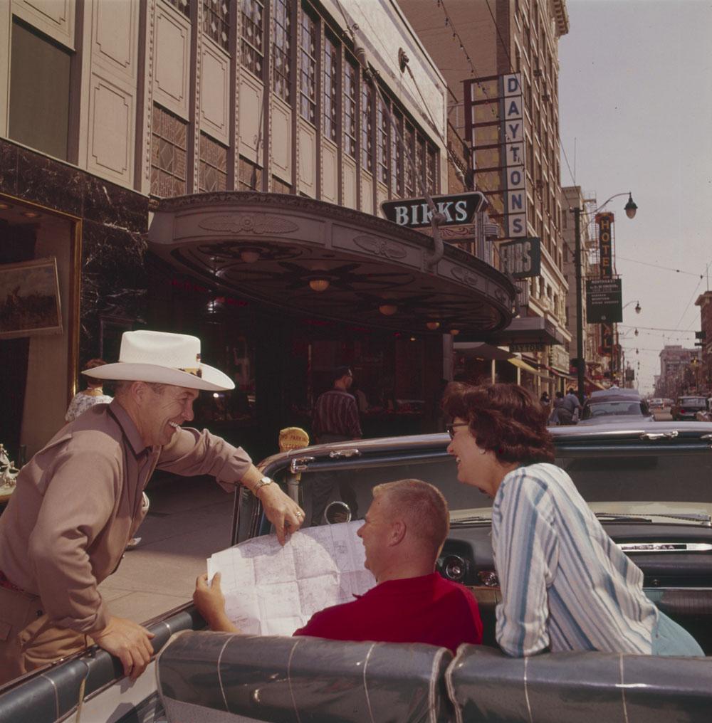 Tourists sightseeing from convertible car in downtown Calgary, Alberta, asking directions from Calgarian whitehatter (1961).jpg