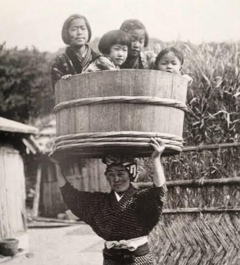 A Japanese woman carrying her children in a bucket on her head, 1900s.jpg