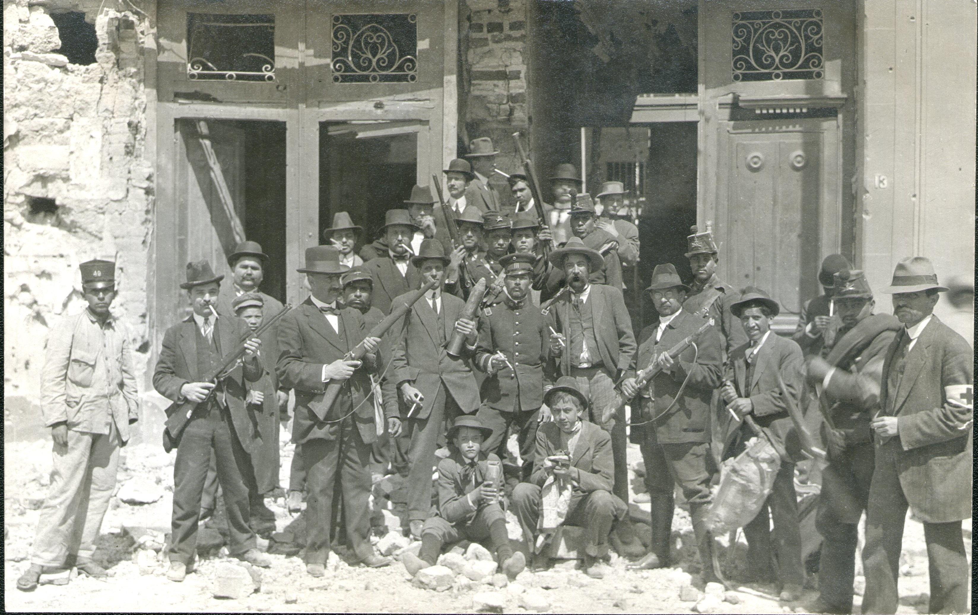 Mexico city, Mexico 1913 (Feb) post 'Decena Tragica'. Group of journalists, red cross, civilians and soldiers, in front of one affected building with captured weapons. Love the guy who decided to grab the huge shell.jpeg