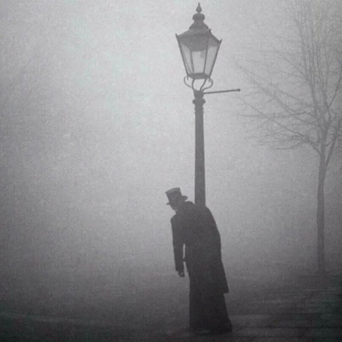 A drunk man in a top hat clings to a lamp-post in London, 1934 Photo is by Bill Brandt.png