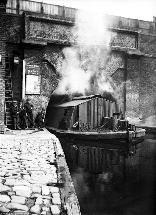 River boat sailing under a bridge or tunnel on the Regent’s Canal, as workers stand next to it - London, England, United Kingdom, c. 1905.jpeg