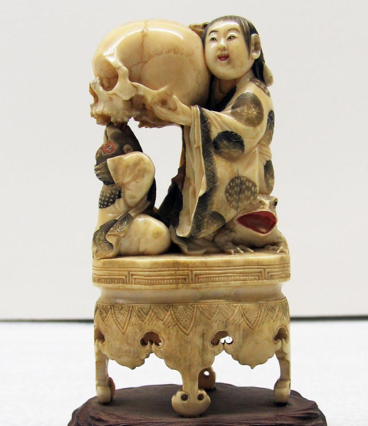 Ivory carving of a lady sitting on a frog holding a skull with a monkey seated in front of her. Japan, Edo period, 18th century.jpeg