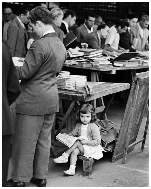 Captured in 1955 by Ramon Masats, a young girl sits quietly beneath a table at an outdoor book market in Barcelona, Spain.jpg