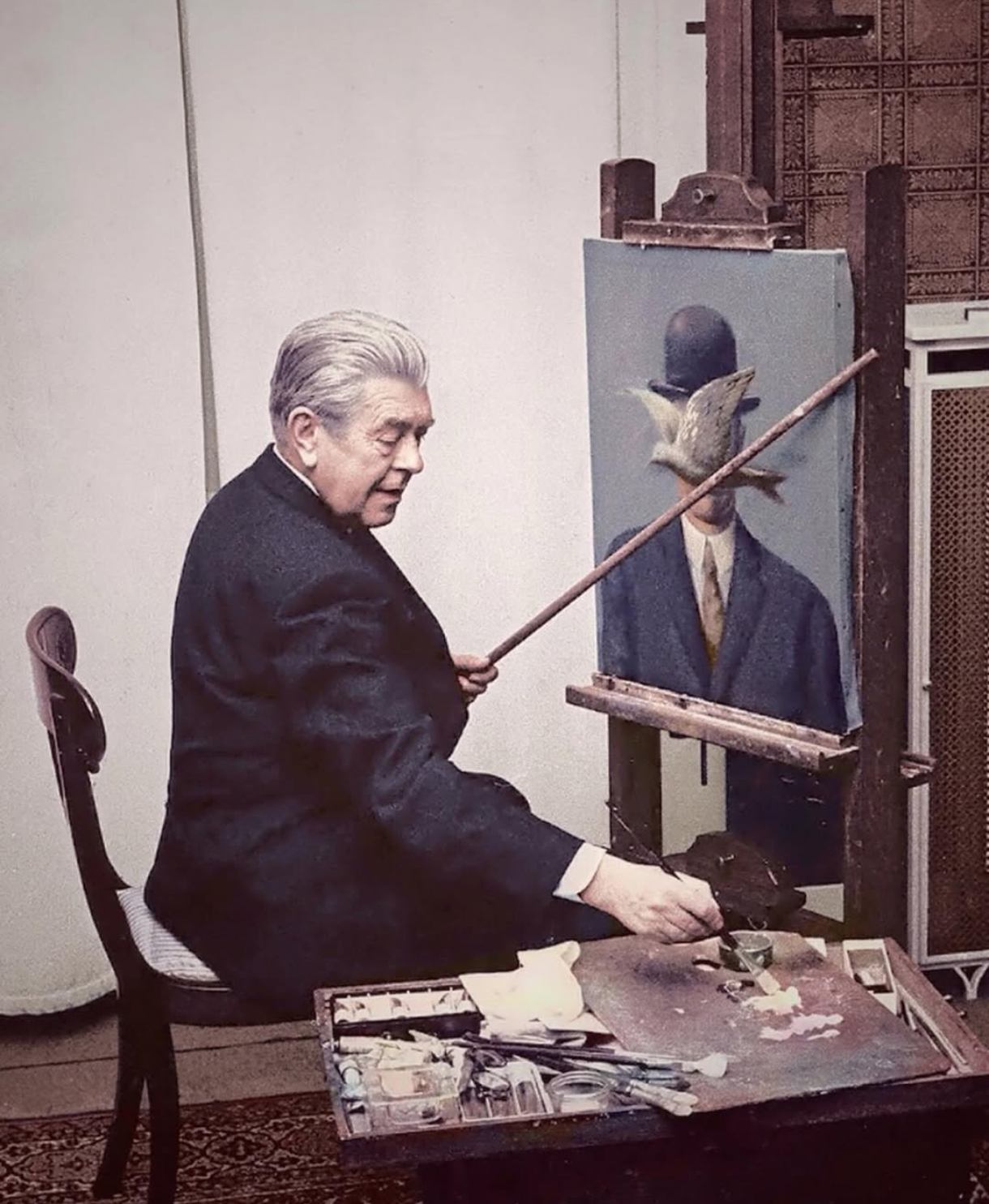 Belgian Surrealist painter, René Magritte, at work in his living room in 1964.png